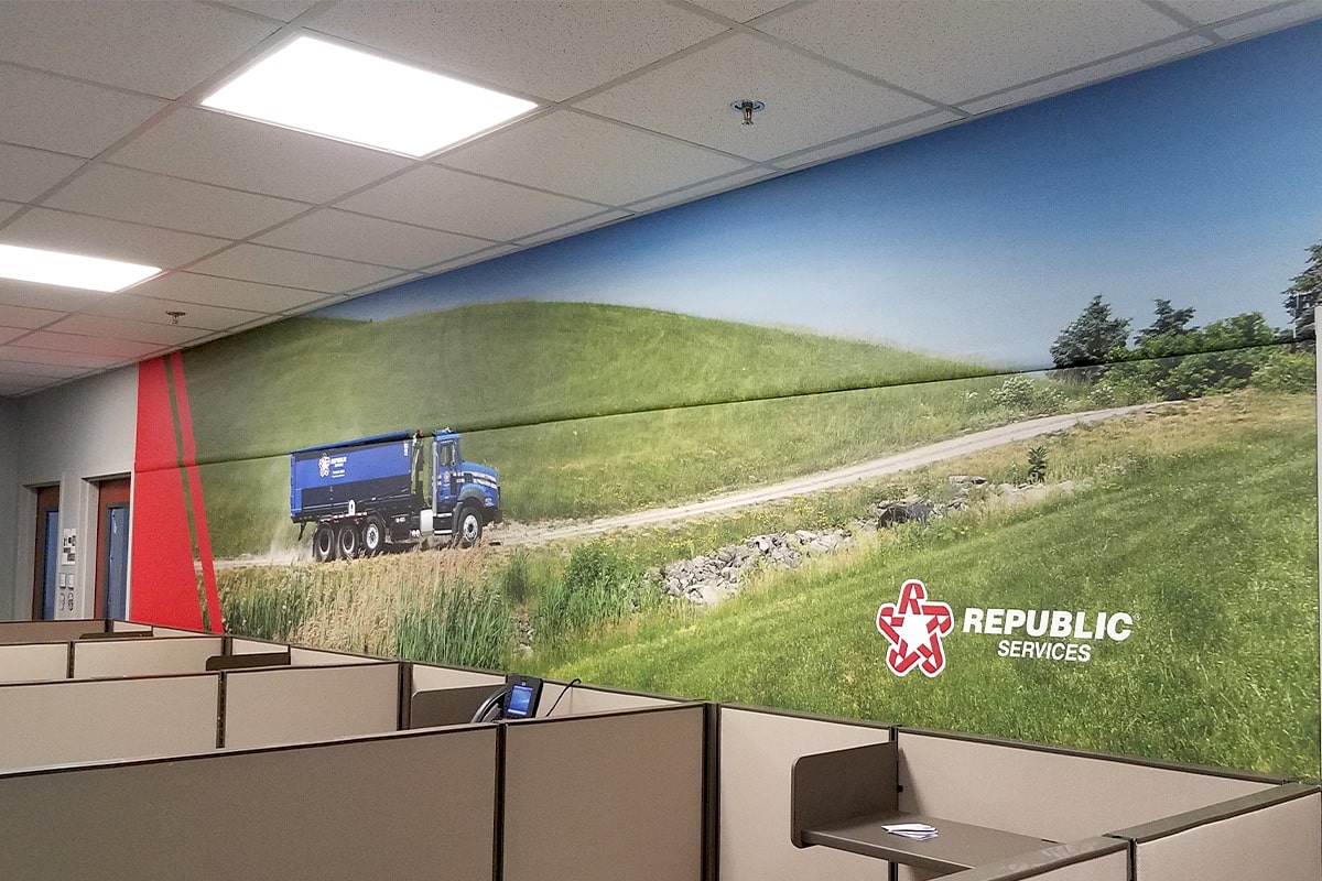 A vibrant wall mural by Image Craft, displayed in an office setting, features a Republic Services truck driving along a picturesque country road, with the company's logo prominently placed on a backdrop of rolling green hills, symbolizing its commitment to environmental sustainability.