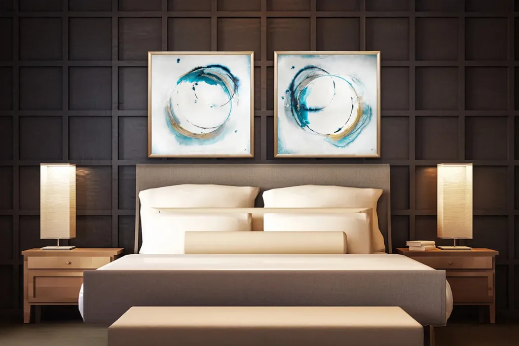 Two framed abstract pieces of art hung above a bed in a hotel room.