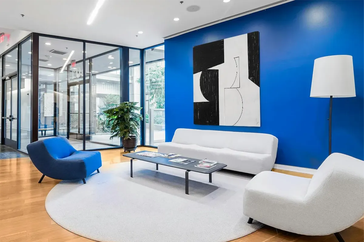 Monochrome abstract canvas artwork on a bold blue wall in a contemporary office lounge area with modern white seating and wood floors.