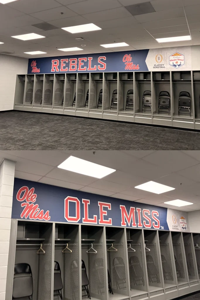 Interior of a football locker room with rows of open gray metal lockers and folded chairs inside. Above the lockers, bold Ole Miss Rebels signage spans the wall, with ‘REBELS’ and ‘Ole Miss’ lettering alongside College Football Playoff Semifinal and Vrbo Fiesta Bowl logos under bright ceiling lights.